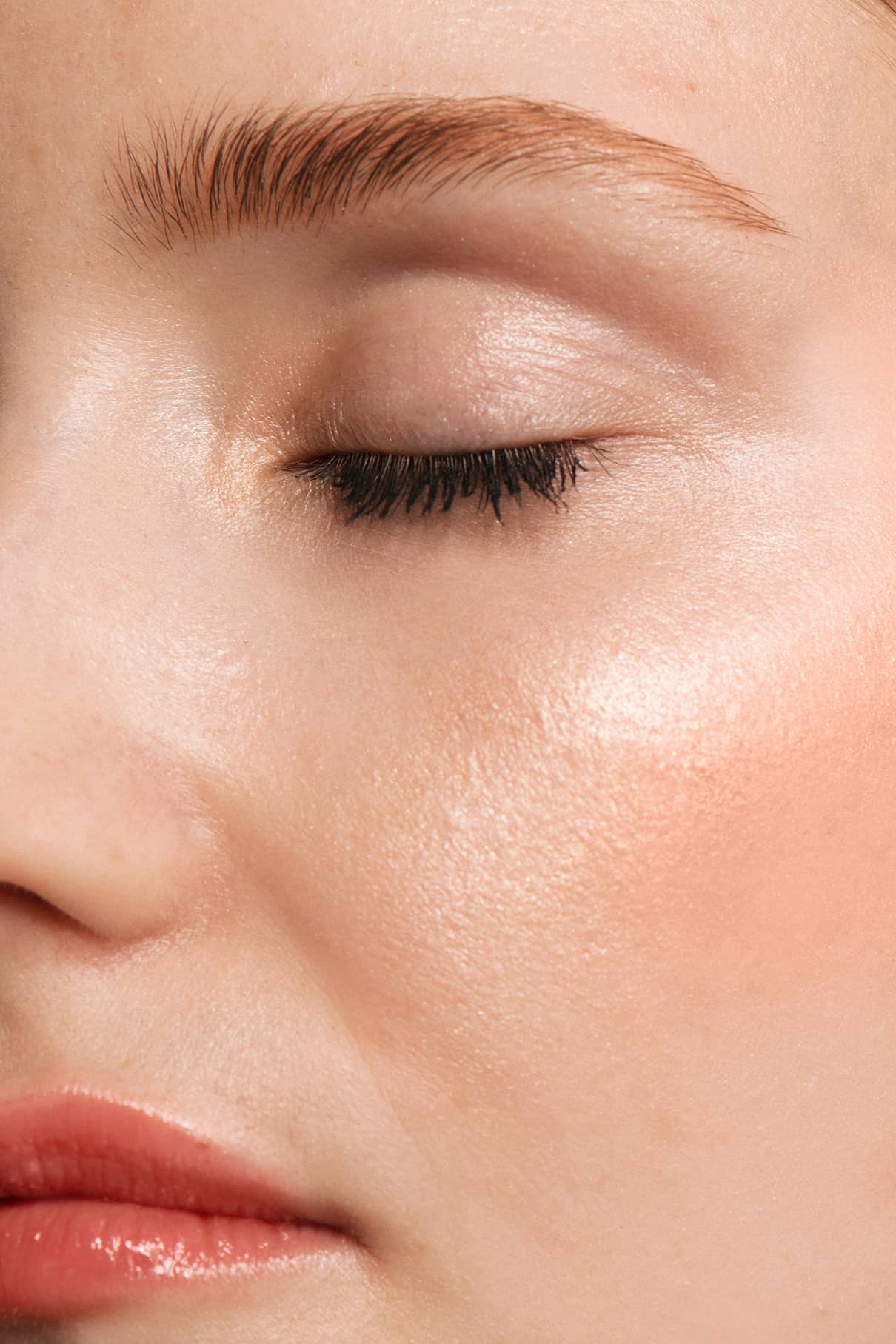 Eine Nahaufnahme des Gesichts einer Person mit geschlossenen Augen, glatter Haut, samtigen Wangen und einem subtilen Make-up, das durch das Signature Set verstärkt wird, das natürliche Augenbrauen und einen schimmernden Lippenstift hervorhebt.