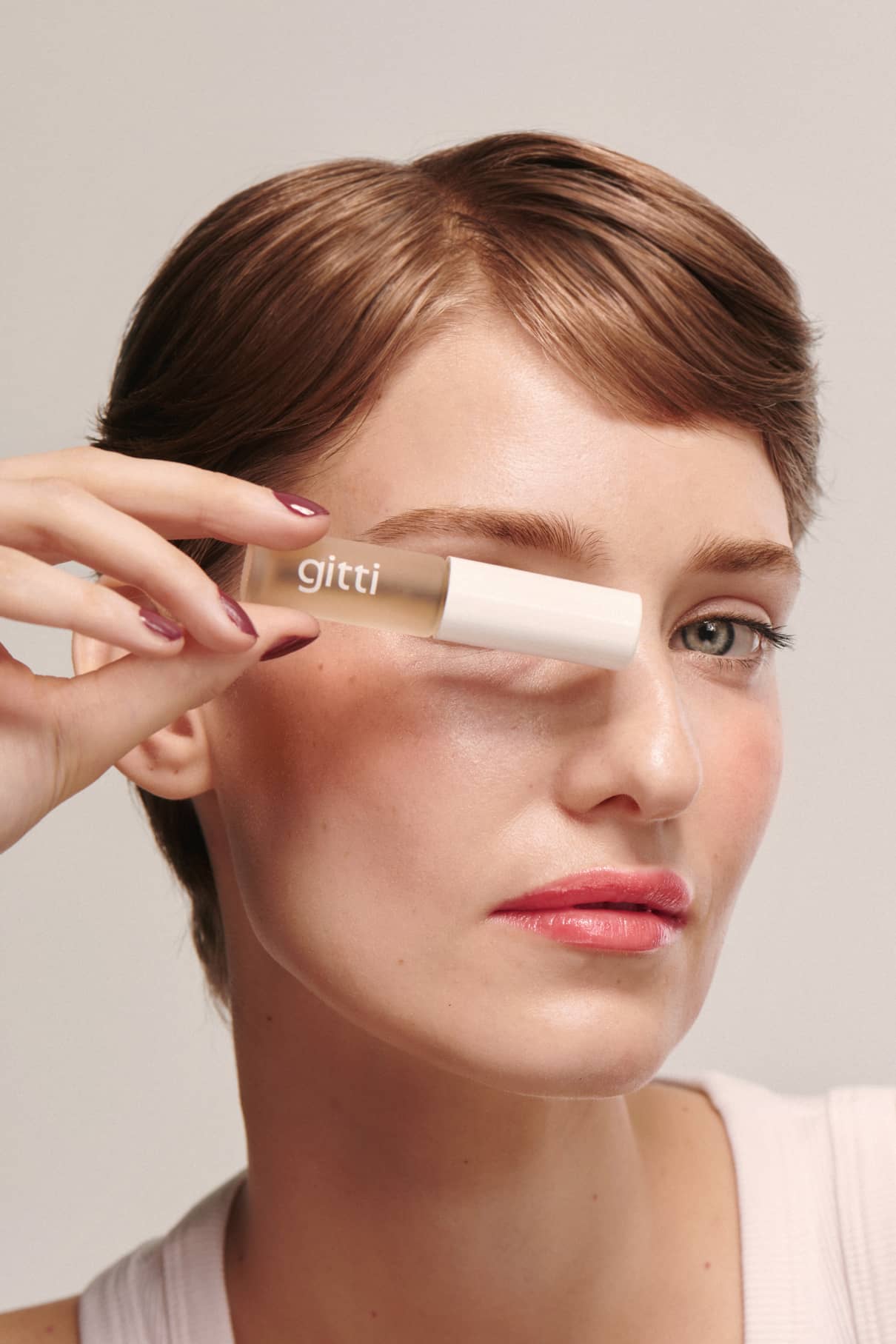 Eine Person mit kurzen braunen Haaren hält ein Brow Control Gel mit einer leichten Textur vor ihr rechtes Auge und zeigt einen neutralen Gesichtsausdruck.