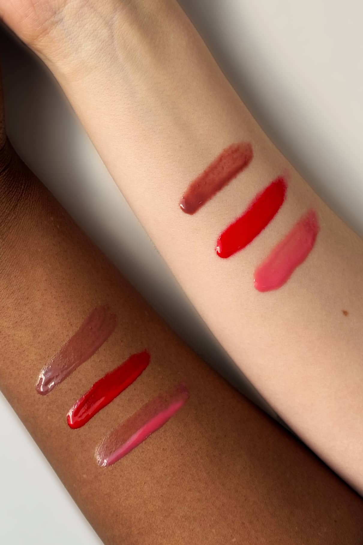 Zwei Arme mit unterschiedlichen Hauttönen zeigen drei Swatches - braun, leuchtend rot und pink - unserer Lip Glaze Nr. 03 für ein hochglänzendes Finish, alle vor einem neutralen Hintergrund.