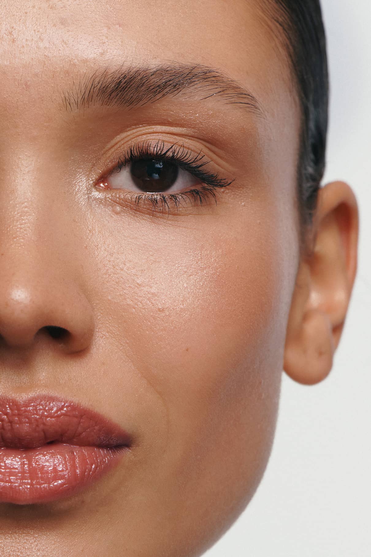 Nahaufnahme eines Frauengesichts mit glatter, silikonfreier Haut, braunen Augen, natürlichem Make-up und einem Hauch von Velvet Cheeks no. 01 in Beerenrot auf den Wangen; die Lippen sind leicht gescheitelt.