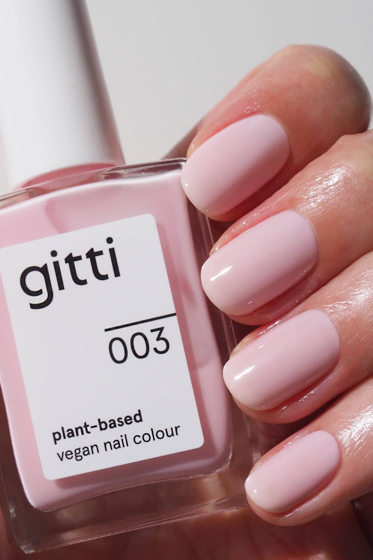 Eine Hand mit sauber manikürten hellrosa Nägeln hält ein Fläschchen aus der Plant Collection, einer pflanzlichen, veganen Nagelfarbe in einem passenden Farbton - ideal zum Kombinieren mit Unter- oder Überlacken für ein lang anhaltendes Finish.