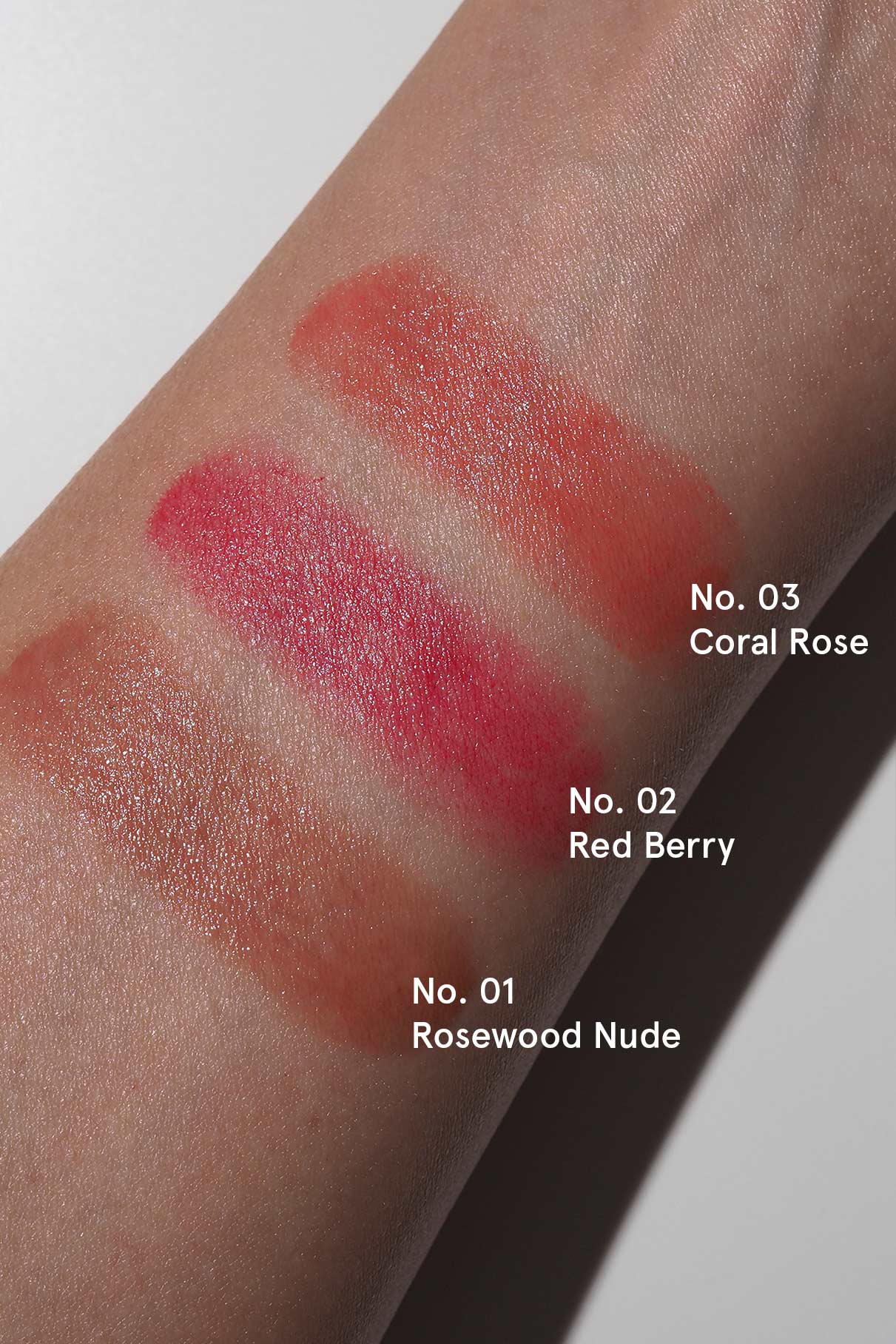 Swatches der Celebration Trio-Farbtöne Nr. 01 Rosewood Nude, Nr. 02 Red Berry und Nr. 03 Coral Rose werden auf einem Unterarm in natürlichem Licht gezeigt, ergänzt durch Ihre Lieblings-Mascara für ein makelloses Finish.