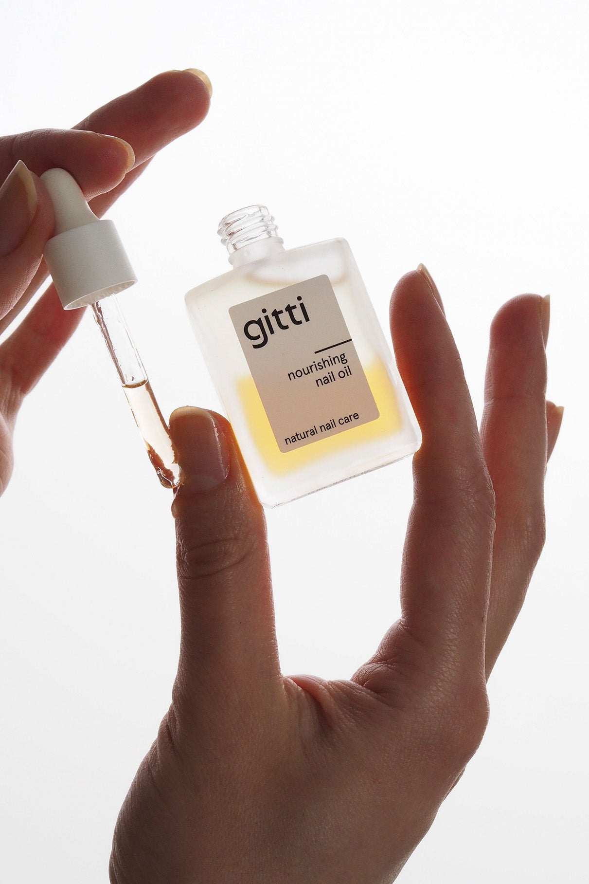 Eine Hand hält eine Flasche Be A Softie, während die andere eine Pipette benutzt, um das Öl zu verteilen - perfekt, um es mit Ihrer Lieblingshandcreme für ein komplettes Nagel- und Hautpflegeset zu kombinieren.